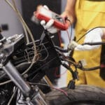 mécanicien procédant à un diagnostic suite à une panne électrique sur une moto en utilisant un multimètre digital