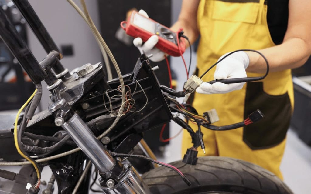 mécanicien procédant à un diagnostic suite à une panne électrique sur une moto en utilisant un multimètre digital